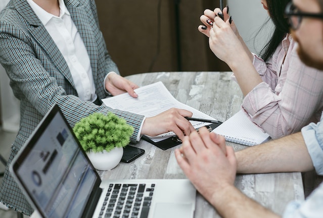 person going over a document with two other people as they compare financial information on their laptop